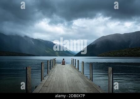 One man sitting on the jetty and watching the storms at Lake Rotoiti, Nelson Lakes National Park. Stock Photo