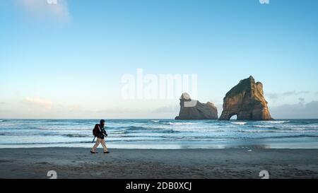 Walking on the beach with Archway Islands in the distance at Wharariki Beach, Cape Farewell, the northernmost point of the South Island of New Zealand Stock Photo