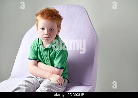 Cute red haired freckled little boy in green t-shirt waiting for doctor in medical office Stock Photo