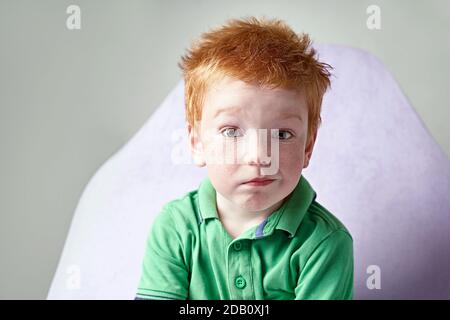 Cute red haired freckled little boy in green t-shirt waiting for doctor in medical office Stock Photo