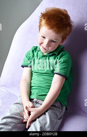 Cute red haired freckled little boy in green t-shirt waiting for doctor in medical office Stock Photo