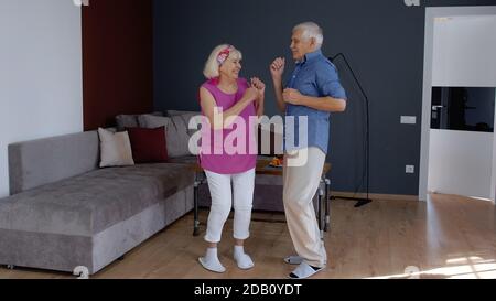 Happy senior couple dancing laughing at home. Beautiful romantic elderly grandparents relaxing having fun together celebrating anniversary enjoy care love tenderness Stock Photo