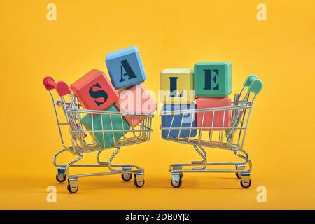 A miniature shopping cart and multi-colored cubes on yellow background. Sales word written on cubes. Stock Photo