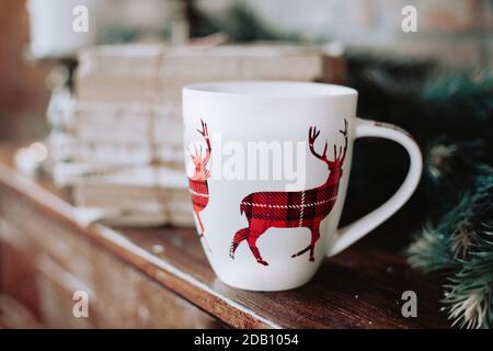 Christmas mug with a red checkered reindeer on a fireplace with vintage books. Rustic, cozy, winter Christmas mood. Stock Photo