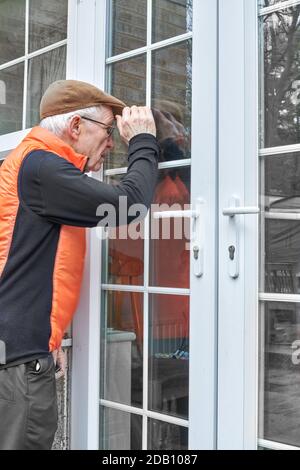 Elderly man looks through a door and window from outside. Stock Photo