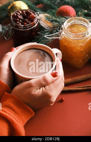 Closeup female hands holding hot chocolate near jam jars. Sweet breakfast Christmas morning Stock Photo