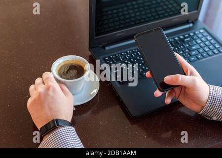 Remote work. Man using laptop, holding smart phone for business work or study in smart watch drink coffee. Freelancer work space. Close up remote work Stock Photo