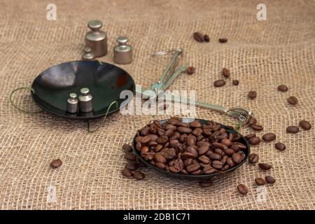 Roasted coffee beans, weighed on an antique hand scale with weights, lying on a table covered with burlap. Stock Photo