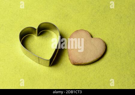 Homemade cookies with a metal baking dish in the shape of a heart on a yellow background. Selective focus. Stock Photo