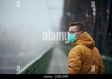Lonely with face mask looking back during walking on bridge in fog. Themes life in new normal, coronavirus and personal protection. Stock Photo