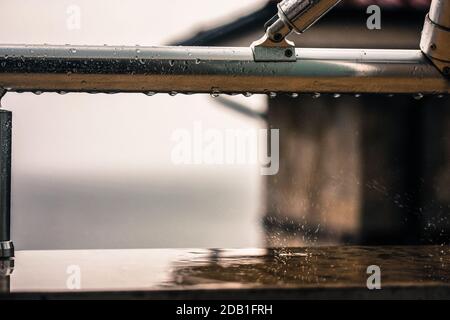 Rain drops on the balcony metal railing close-up after the rain, view from the window. Stock Photo