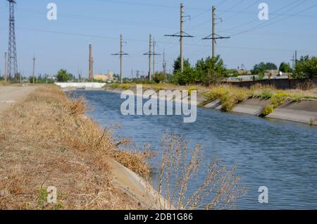 Irrigation agricultural channel with water. Power line along the canal for irrigation. Summer sunny day. Agribusiness. Stock Photo