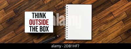 lightbox with message THINK OUTSIDE THE BOX with a notepad on wooden floor Stock Photo