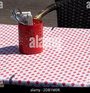 Retro style diner in red. Outdoor cafe terrace with checkered tablecloth covering table and utensil setting in metal pot. Wicker chair on sidewalk pav Stock Photo