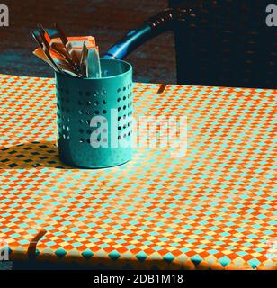 Retro style diner. Toned photo. Outdoor cafe terrace with checkered tablecloth covering table and utensil setting in metal pot. Wicker chair on sidewa Stock Photo