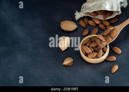 Almonds in a wooden bowl and on a wooden spoon on a black wooden table. some fruits are in a cotton mesh eco bag Stock Photo