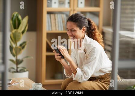 Portrait of elegant adult woman looking at smartphone screen and laughing while chatting online with friends and family, copy space Stock Photo