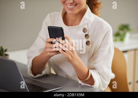 Cropped portrait of smiling young woman using smartphone at workplace while enjoying work from home, copy space Stock Photo