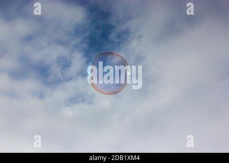 Round rainbow soap bubble colorful close-up against the blue sky. Children's entertainment and fun in summer. Stock Photo