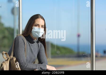 Girl wearing a mask preventing contagion sitting waiting in a bus stop Stock Photo