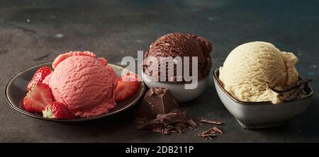 Scoops of chocolate, strawberry and vanilla ice-cream in individual bowls with fresh fruit, candy and vanilla pods for flavoring in a panorama banner Stock Photo