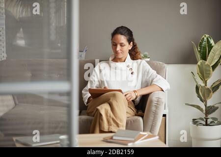 Portrait of modern successful businesswoman using digital tablet while relaxing on couch in office, copy space Stock Photo