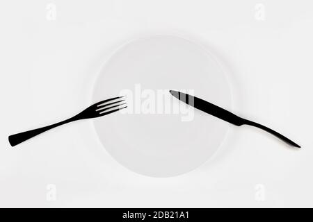 Cutlery language, dining etiquette. Pause. White ceramic round plate with knife anf fork isolated on white, top view. Stock Photo