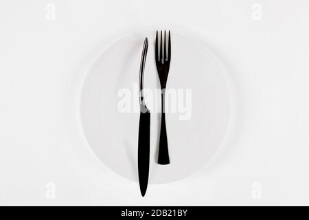 Cutlery language, dining etiquette. White ceramic round plate with knife anf fork isolated on white, top view. Stock Photo