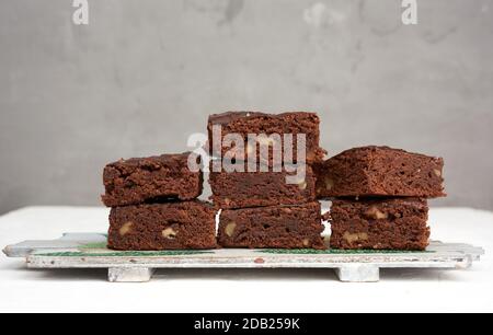 stack of square baked pieces of brownie chocolate cake with walnuts, on a wooden board Stock Photo