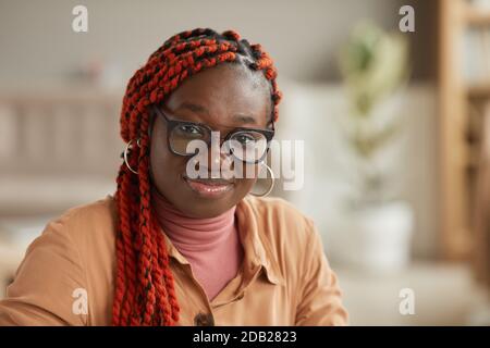 Close up portrait of young African-American woman wearing glasses and smiling at camera against blurred home or office background, copy space Stock Photo