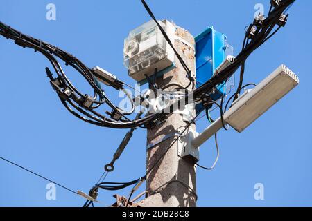 Top of a power pole with street light, electric meter and wires is under cloudy sky at day Stock Photo