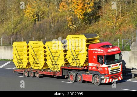 Haulage business lorry truck & low loader delivery trailer loaded with stacks of twenty new unused yellow steel rubbish skip driving on UK motorway Stock Photo