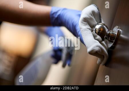 Close up of maid in gloves and wiping the door handle while using special disinfectant. Hotel service concept Stock Photo