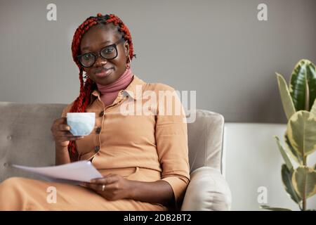 Portrait of young African-American woman holding coffee mug and smiling at camera while enjoying work from home office, copy space Stock Photo