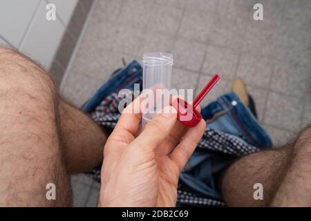 Stool Sample Container In Hands Of Man Sitting On Toilet Stock Photo