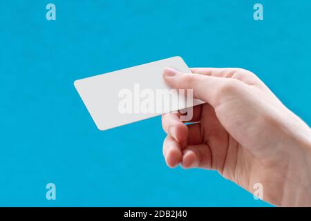 Close up of a female hand holding a blank white business card on a blue background. Business idea, copy space. Stock Photo