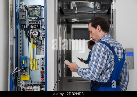 Technician Repairing Control Panel Of Broken Elevator Stock Photo