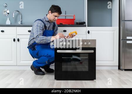 Young Male Technician Checking Oven With Digital Multimeter Stock Photo