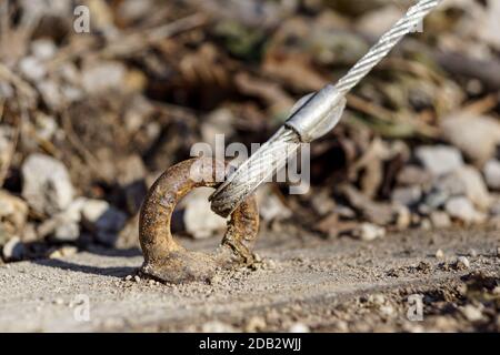 Generic eyelet and steel cables to guy ropes to strengthen a building structure, green leafy background, sunny day. Rusty metal which has been greased Stock Photo