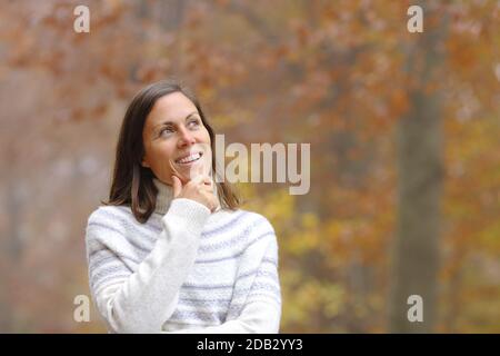 Pensive middle age woman standing in a forest looking at side in autumn Stock Photo
