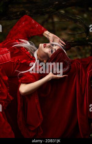 Maleficent Woman in Red Clothing and Horns in dark Forest. Posing in magik forest Stock Photo