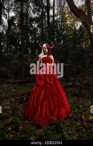 Maleficent Woman in Red Clothing and Horns in dark Forest. Posing in magik forest Stock Photo