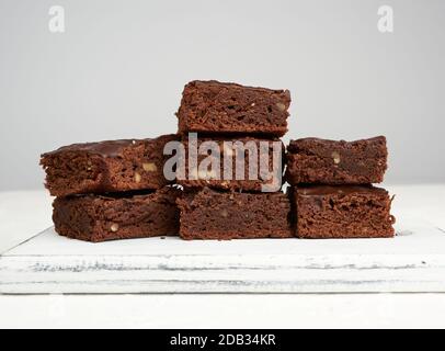 stack of square baked slices of brownie chocolate cake with walnuts on a white wooden board Stock Photo