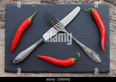 Red chilies and old silver cutlery on a black slate tray Stock Photo