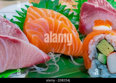 Japanese food set served on white plate. Salmon sushi and sashimi on restaurant table. Fresh raw fish meat sliced and Japan vinegared rice rolls with