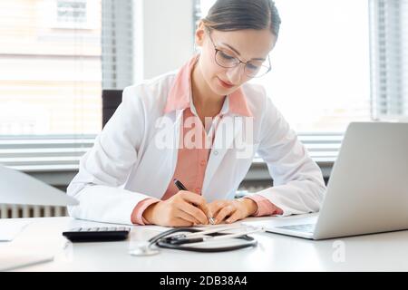 Doctor doing office works and administration on the desk in her office writing Stock Photo