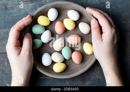 Hands holding stylish pastel painted easter eggs in ceramic grey plate on vintage old wooden background, Happy Easter concept Stock Photo