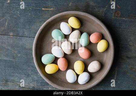 Grey Ceramic Plate with painted Easter Eggs of pastel colors on vintage wooden background. Happy Easter card concept, minimalistic design, top view Stock Photo
