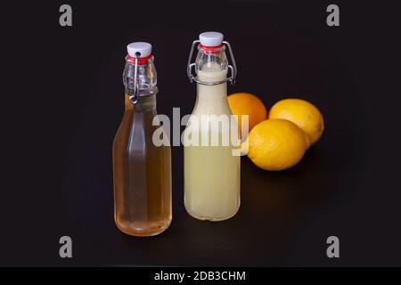 Two flip-top patent closure bottles with homemade lemon syrup or juice and three lemons on black background. Stock Photo