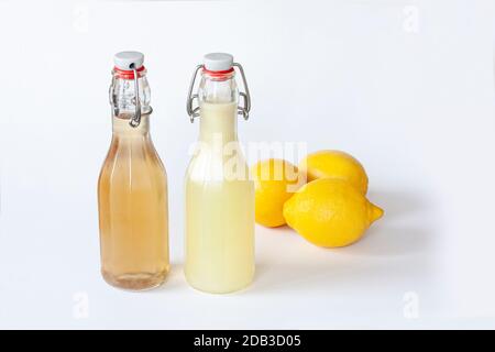Two flip-top patent closure bottles with homemade lemon syrup or juice and three lemons on white background. Stock Photo
